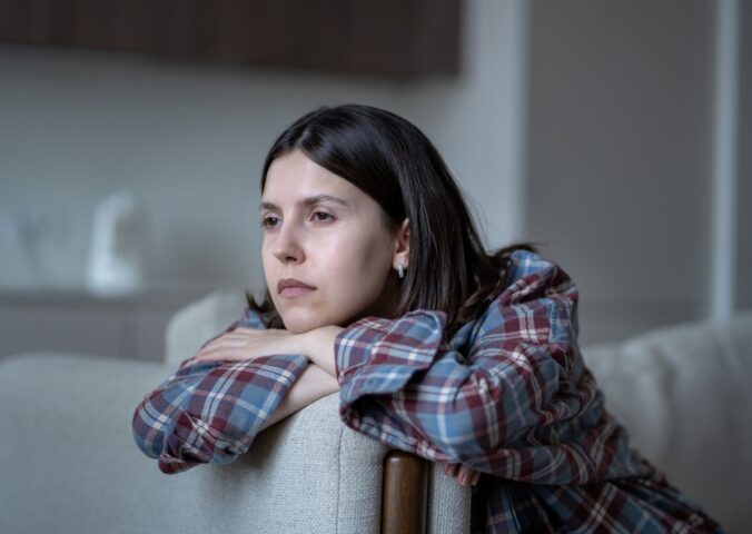 Pale woman sitting on a couch looking listlessly out the window, illustrating symptoms of low iron for article on how to fix low iron.