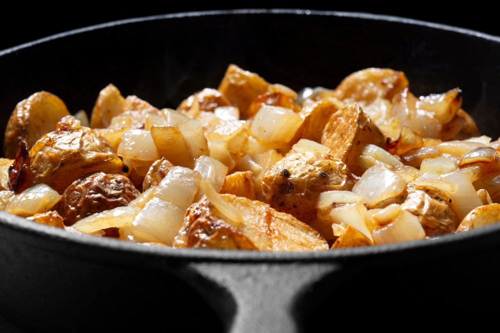 Fried crispy chopped potato and onion cooked in a cast iron frying pan on a black background, to illustrate article on how to fix low iron