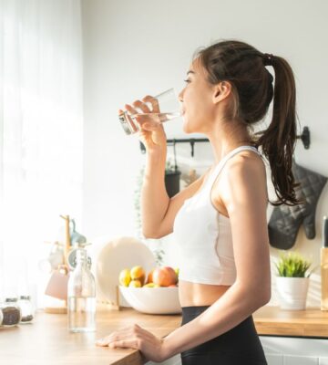 Woman in sportswear drinking water in the kitchen, showing that hydration is one of 8 daily habits to reduce inflammation