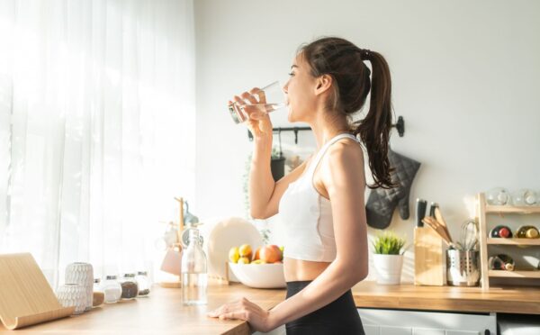 Woman in sportswear drinking water in the kitchen, showing that hydration is one of 8 daily habits to reduce inflammation