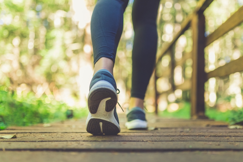 A woman’s legs wearing running shoes on a wooden footpath in a forest, illustrating one of the daily habits to reduce inflammation
