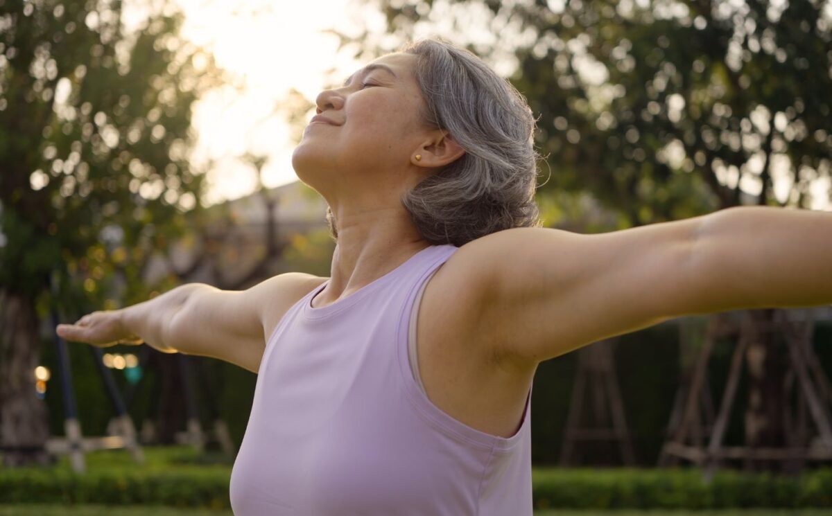 Middle-aged woman practicing yoga in a park, looking happy and inspired, to illustrate article about gut health during perimenopause