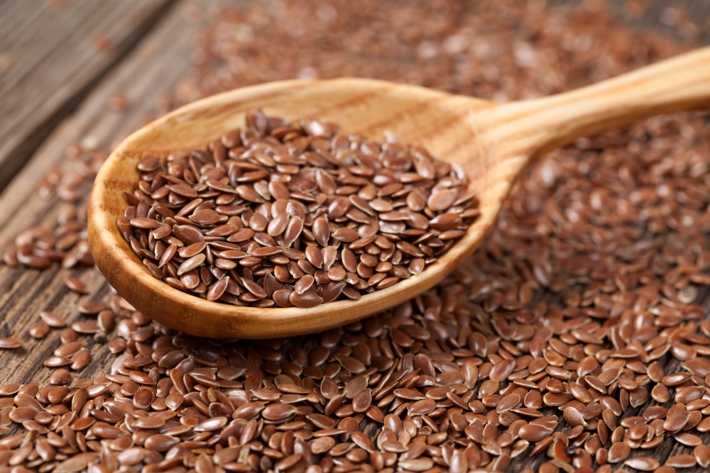 Heap of flax seeds in wooden spoon and spilled over a wooden table to illustrate an article about gut health during perimenopause