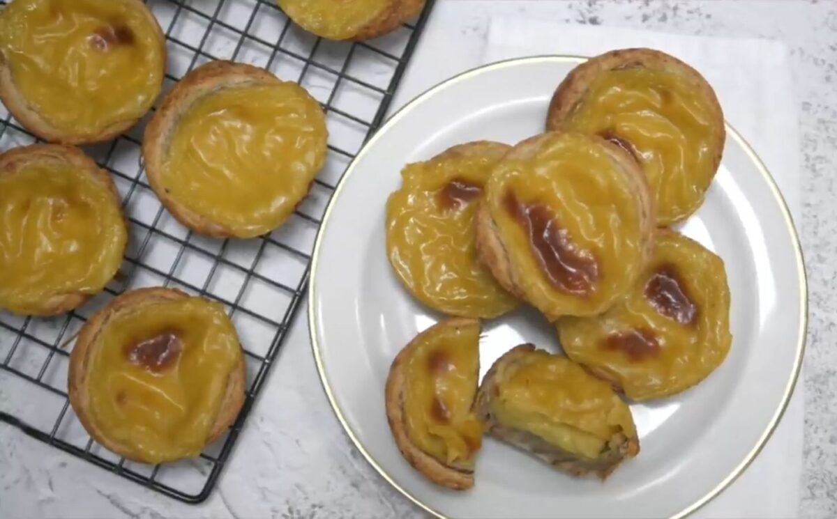 Freshly baked vegan Portuguese custard tarts on a plate and on a black wire baking rack