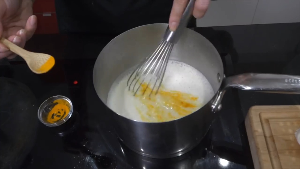 Hutchings adds turmeric to a pot of custard mixture while making vegan Portuguese custard tarts