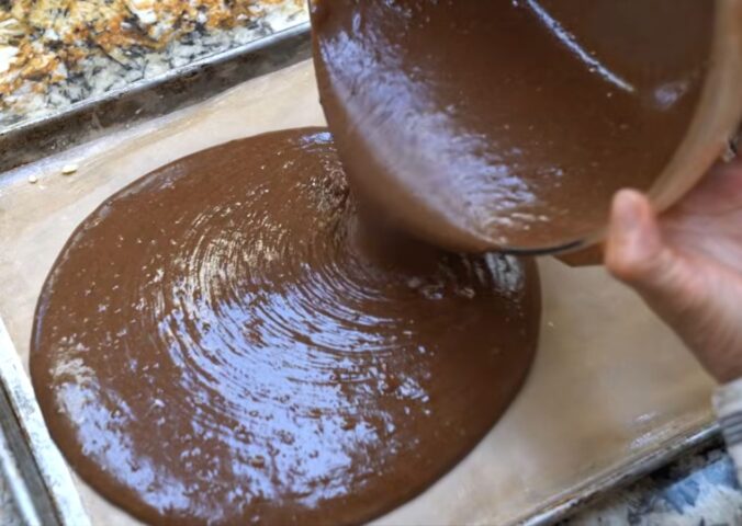 Schinner pours the cake batter, made using her vegan chocolate cake mix, from a bowl onto a baking tray
