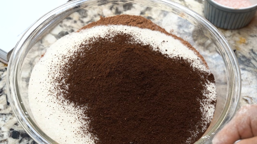 Finely ground coffee on top of vegan chocolate cake mix in a bowl with other visible ingredients like sugar, flour and cocoa powder