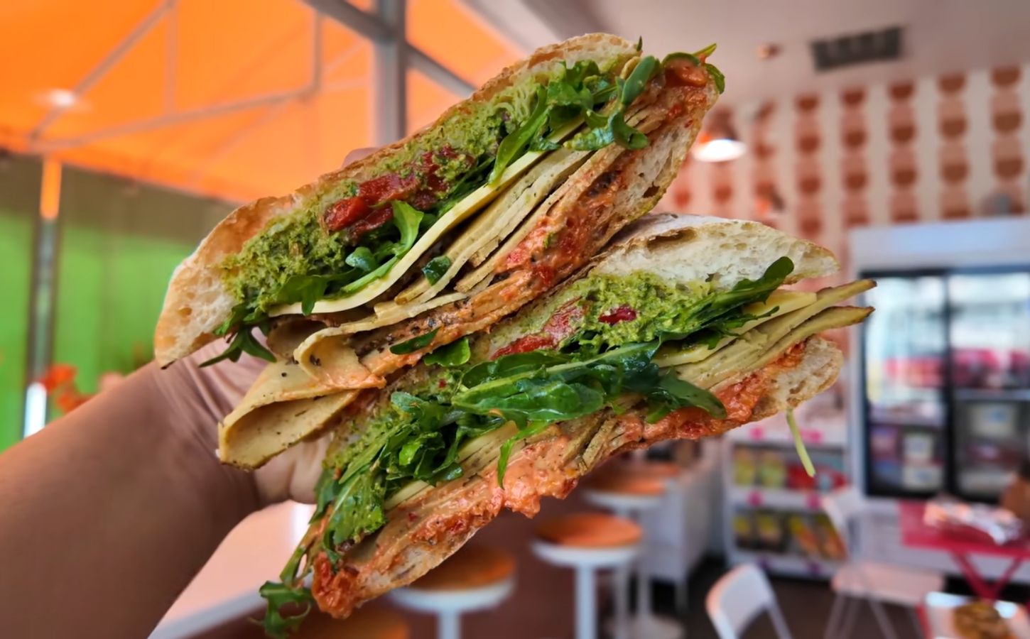 Reyes holding a sandwich at Maciel's Plant-Based Butcher Shop with the deli in the background, to illustrate an article about the award-winning vegan sandwiches in LA