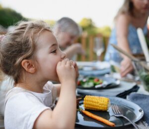 Photo shows a little girl eating corn on the cob and vegetables at a family BBQ. A new study has found that children and teenagers are more open to meat-free diets than adults, but can struggle to maintain them