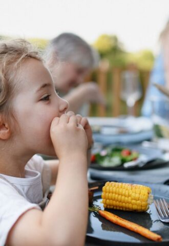 Photo shows a little girl eating corn on the cob and vegetables at a family BBQ. A new study has found that children and teenagers are more open to meat-free diets than adults, but can struggle to maintain them