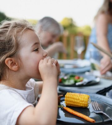 Photo shows a little girl eating corn on the cob and vegetables at a family BBQ. A new study has found that children and teenagers are more open to meat-free diets than adults, but can struggle to maintain them