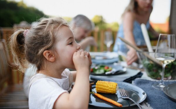 Photo shows a little girl eating corn on the cob and vegetables at a family BBQ. A new study has found that children and teenagers are more open to meat-free diets than adults, but can struggle to maintain them