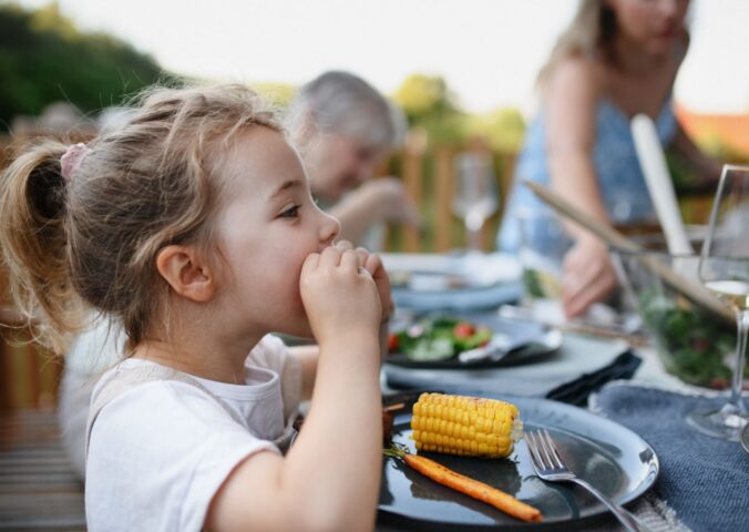 Photo shows a little girl eating corn on the cob and vegetables at a family BBQ. A new study has found that children and teenagers are more open to meat-free diets than adults, but can struggle to maintain them