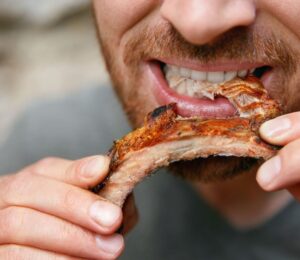 Photo shows a man eating a piece of meat off the bone. A new meta-research review has found that research backed by the animal agriculture industry is more likely to say that meat is beneficial
