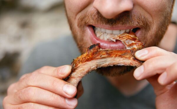 Photo shows a man eating a piece of meat off the bone. A new meta-research review has found that research backed by the animal agriculture industry is more likely to say that meat is beneficial