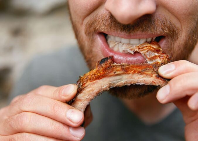 Photo shows a man eating a piece of meat off the bone. A new meta-research review has found that research backed by the animal agriculture industry is more likely to say that meat is beneficial