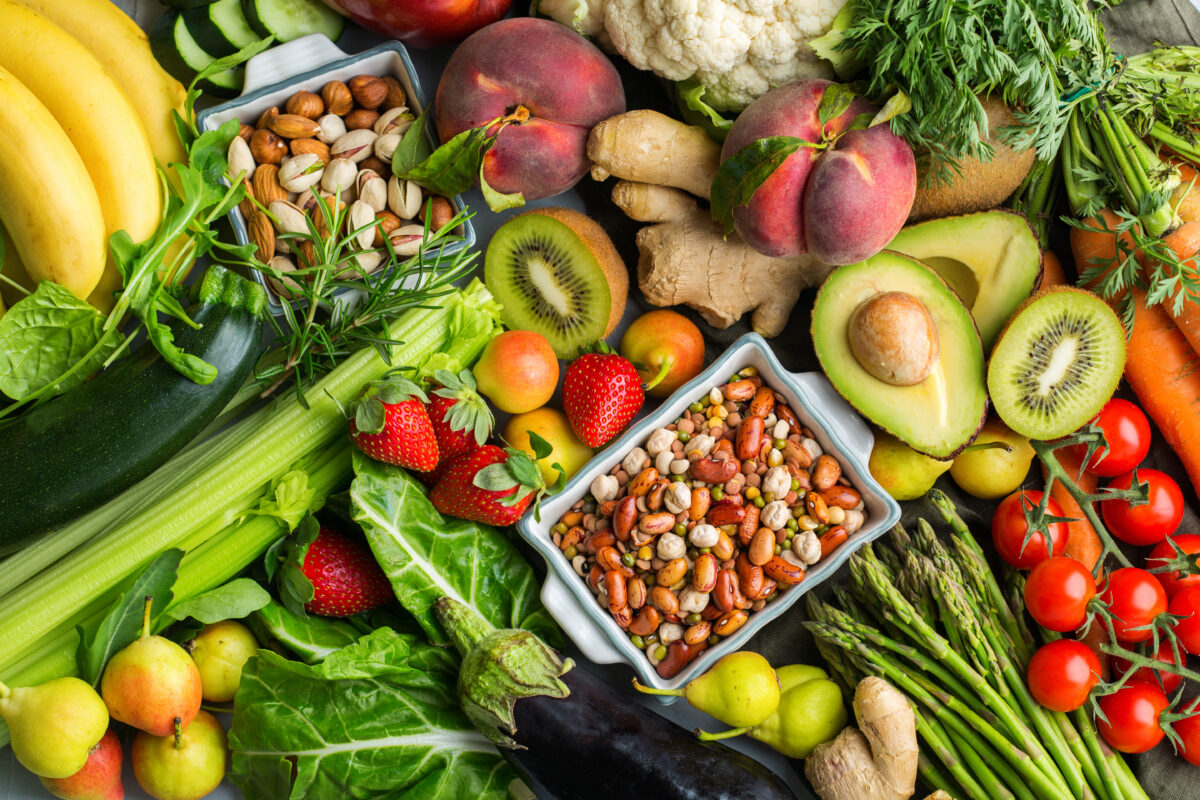 Photo shows an assortment of whole, plant-based foods such as fruits, vegetables, nuts, and seeds.