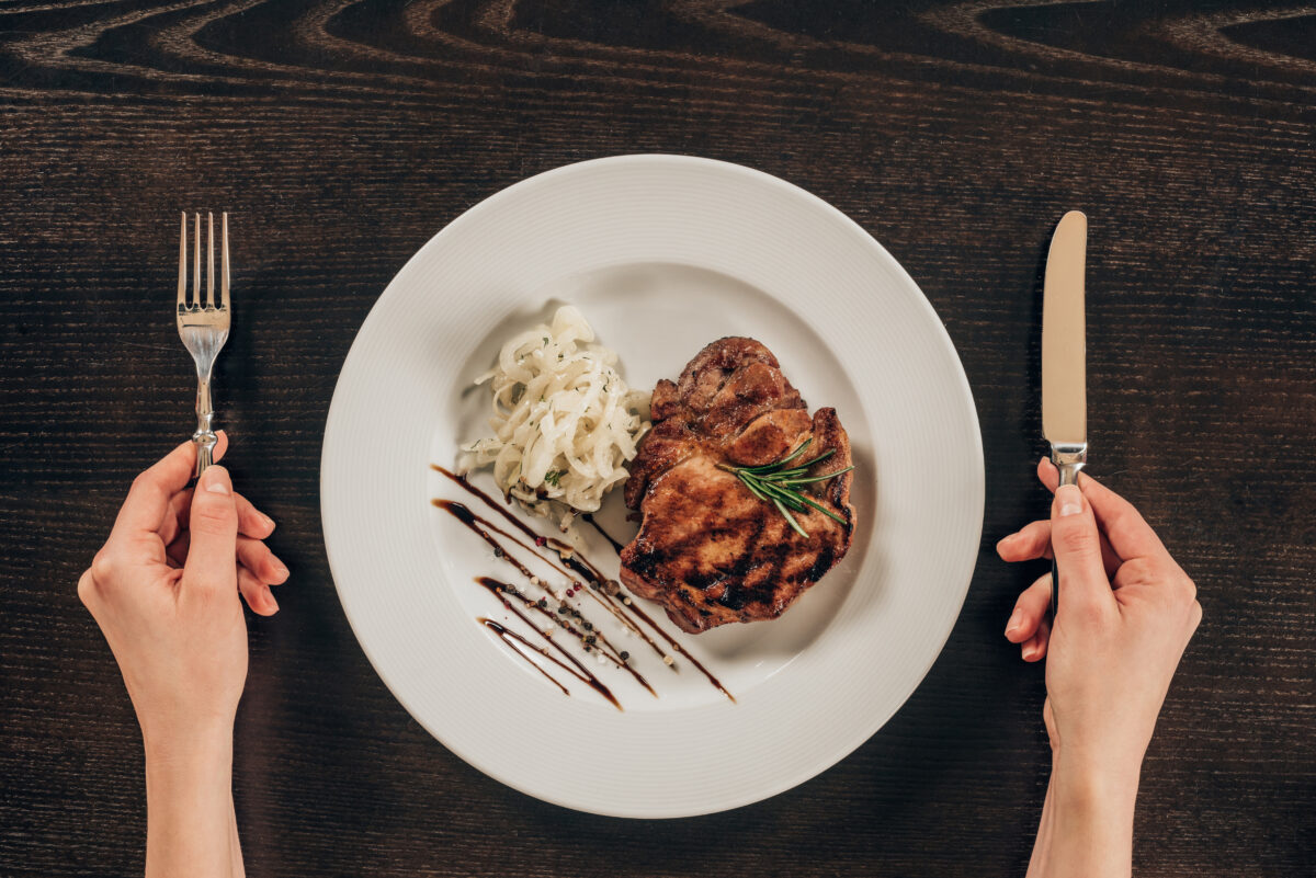 Photo shows a woman's hands holding a fork and knife next to a plate with beef steak on it. Meatly is building Europe’s largest cultivated meat production facility in London, UK