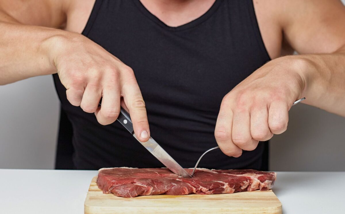 Photo shows a muscular man cutting into a raw steak on a board. A new survey has found that just over half of men perceive meat and the carnivore diet as masculine