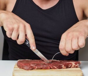 Photo shows a muscular man cutting into a raw steak on a board. A new survey has found that just over half of men perceive meat and the carnivore diet as masculine