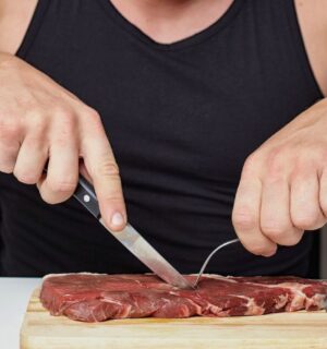 Photo shows a muscular man cutting into a raw steak on a board. A new survey has found that just over half of men perceive meat and the carnivore diet as masculine