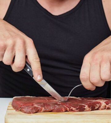 Photo shows a muscular man cutting into a raw steak on a board. A new survey has found that just over half of men perceive meat and the carnivore diet as masculine