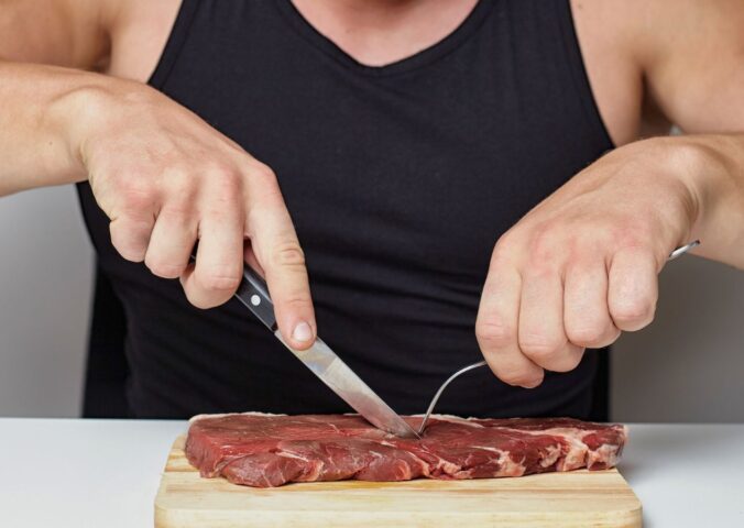 Photo shows a muscular man cutting into a raw steak on a board. A new survey has found that just over half of men perceive meat and the carnivore diet as masculine
