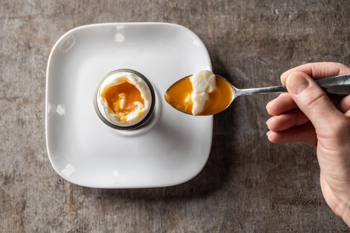 Photo shows a broken soft boiled egg in a cup, and a woman's hand holding a spoonful of the egg. According to a new survey, many US adults incorrectly believe that chicken, beef, and eggs reduce high cholesterol risk
