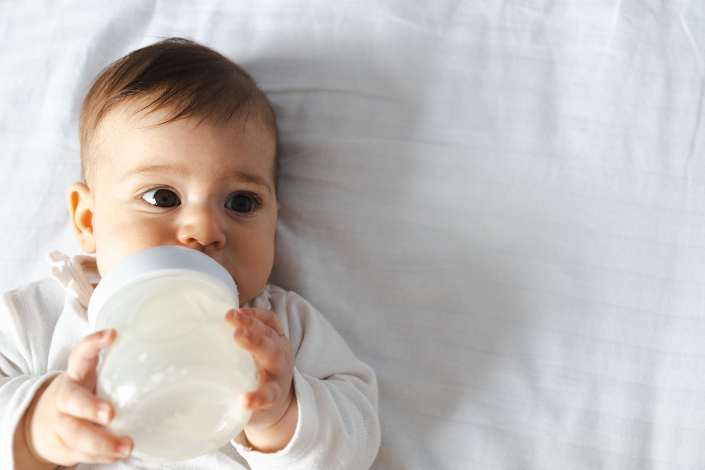 Shot of a cute baby drinking milk from a bottle on white bedding, to illustrate article on how to breathe better