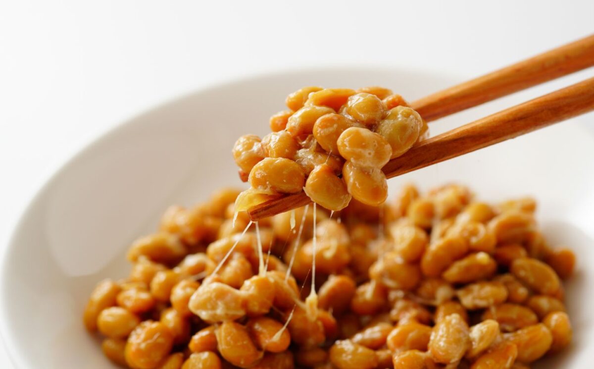 Chopsticks lifting gooey natto out of a white bowl, to illustrate article about nattokinase and artery plaque