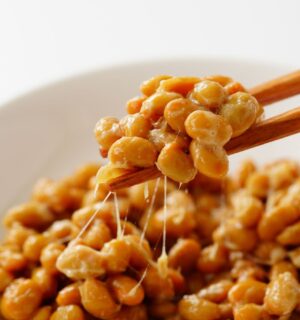 Chopsticks lifting gooey natto out of a white bowl, to illustrate article about nattokinase and artery plaque