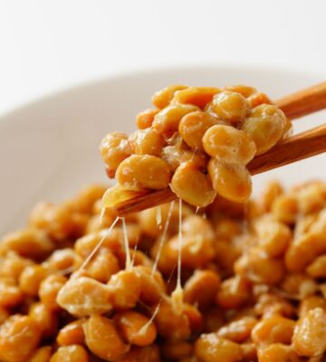 Chopsticks lifting gooey natto out of a white bowl, to illustrate article about nattokinase and artery plaque