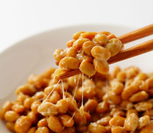 Chopsticks lifting gooey natto out of a white bowl, to illustrate article about nattokinase and artery plaque