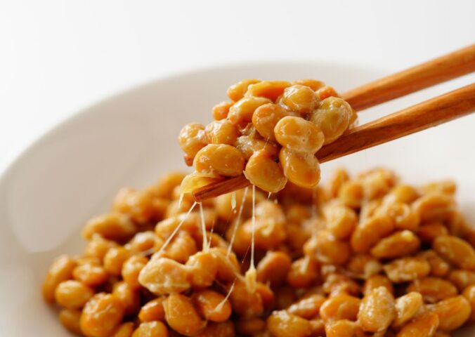 Chopsticks lifting gooey natto out of a white bowl, to illustrate article about nattokinase and artery plaque