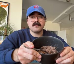 During Eddy Burback's carnivore diet experiment he sits at a table in his apartment holding a bowl of ground beef toward the camera
