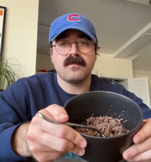 During Eddy Burback's carnivore diet experiment he sits at a table in his apartment holding a bowl of ground beef toward the camera