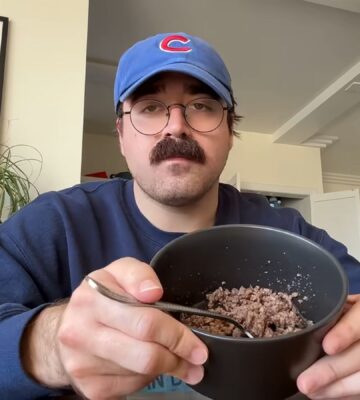 During Eddy Burback's carnivore diet experiment he sits at a table in his apartment holding a bowl of ground beef toward the camera
