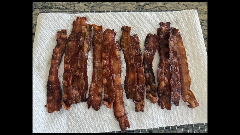 A cooling rack with cooked bacon resting on a paper towel during Eddy Burback's carnivore diet experiment