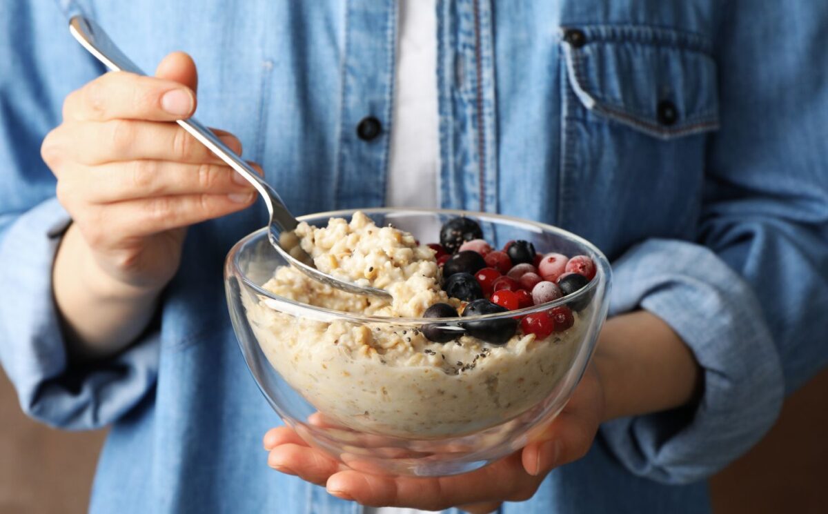 Woman holding a bowl of porridge with berries on the side to illustrate article about the health benefits of oatmeal