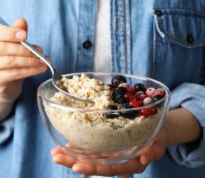 Woman holding a bowl of porridge with berries on the side to illustrate article about the health benefits of oatmeal