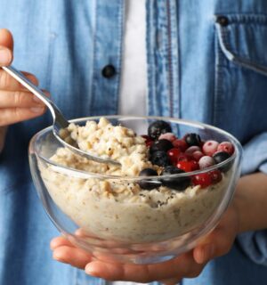 Woman holding a bowl of porridge with berries on the side to illustrate article about the health benefits of oatmeal