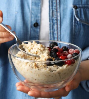 Woman holding a bowl of porridge with berries on the side to illustrate article about the health benefits of oatmeal