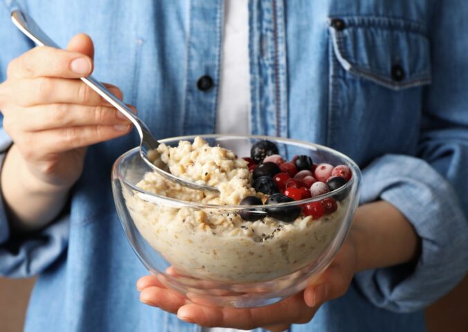 Woman holding a bowl of porridge with berries on the side to illustrate article about the health benefits of oatmeal