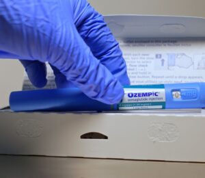 A hand in a blue glove removes an Ozempic injection pen from its box, to illustrate an article about stress eating and weight loss