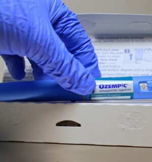 A hand in a blue glove removes an Ozempic injection pen from its box, to illustrate an article about stress eating and weight loss