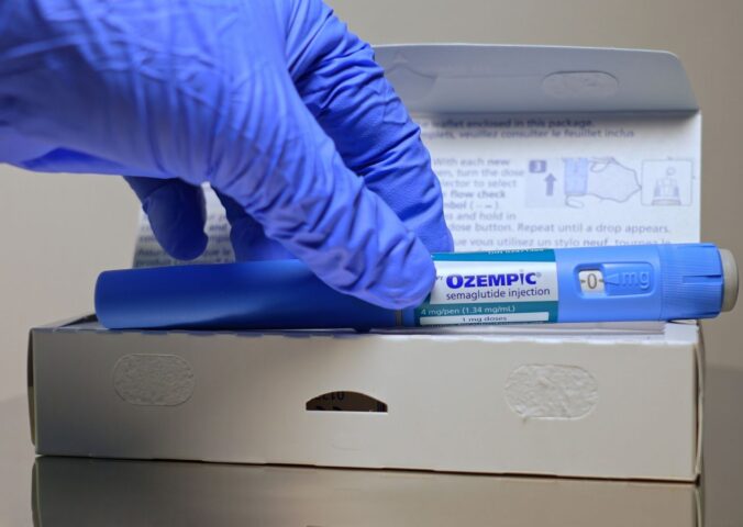 A hand in a blue glove removes an Ozempic injection pen from its box, to illustrate an article about stress eating and weight loss