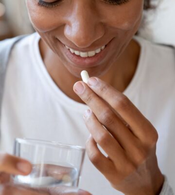 A woman takes a supplement with a glass of water, to illustrate article about using probiotics for gut health correctly