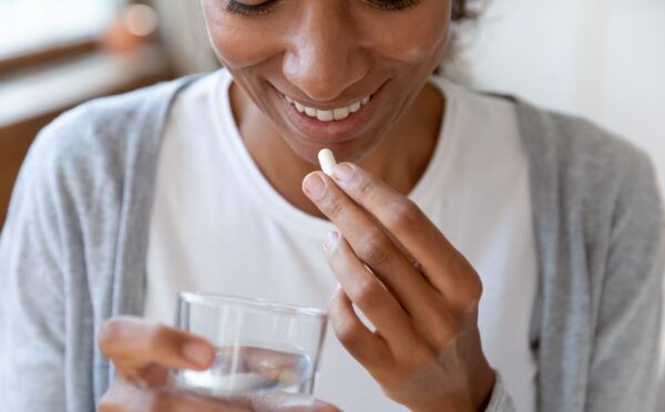 A woman takes a supplement with a glass of water, to illustrate article about using probiotics for gut health correctly