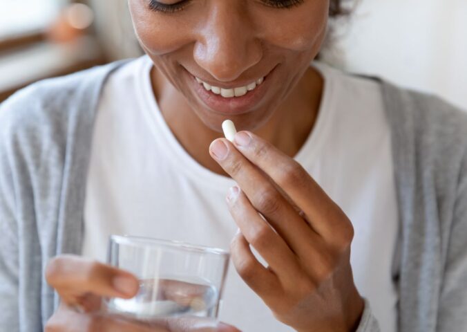 A woman takes a supplement with a glass of water, to illustrate article about using probiotics for gut health correctly