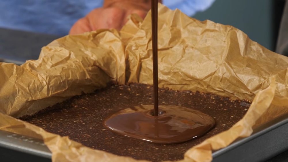 The twins pour melted chocolate over their healthy protein bars in a parchment-lined baking tray